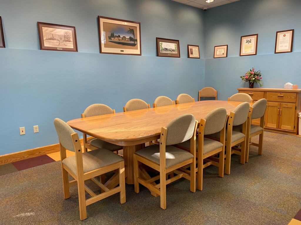 a picture depicting the medium size Mowen room with a large oak table in the middle with 10 chairs around it and two more chairs in the corners of the room